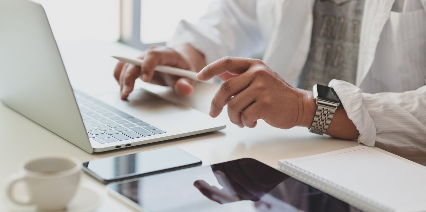 Faceless manager working on laptop at desk with different gadgets and notebook